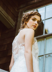Model looking back at camera, showing back detail of sleeveless lace wedding dress.