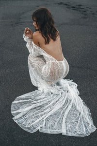 Back view of Model crouching on beach wearing square backless lace wedding dress. 