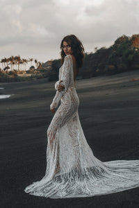 Model standing on beach with her profile showing backless feature of beaded Vancouver wedding dress.