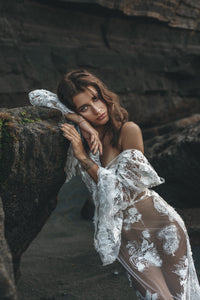 Sexy pose of model showing shoulder leaning against rock in lace wedding dress.