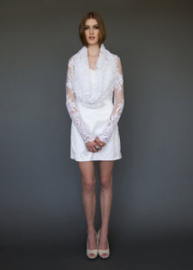 Model standing facing us, in long sleeve lace bridal jacket with draped neckline.