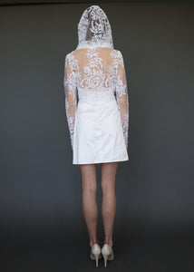 Model facing away, full length, in above knee wedding dress with cowl neck lace bolero jacket.