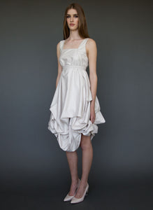 Model full length, side, wearing knee length draped full skirt wedding dress.