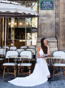 Bride in Paris sitting outside at cafe wearing halter neck wedding dress.