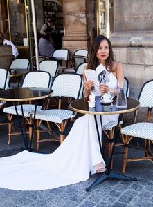 Model in cafe in Paris reading book, wearing backless boho wedding dress.