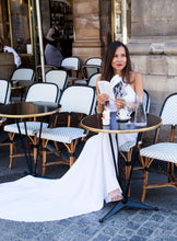 Load image into Gallery viewer, Model in cafe in Paris reading book, wearing backless boho wedding dress.
