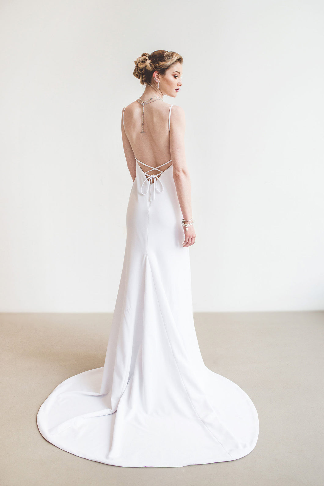 Model, full length from behind, wearing V-neck lace up backless crepe wedding dress.