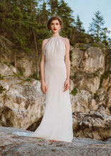 Load image into Gallery viewer, Bride standing on rock wearing backless halter sheath wedding dress by Vancouver bridal designer.
