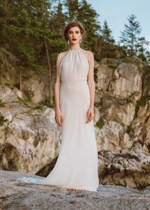 Bride standing on rock wearing backless halter sheath wedding dress by Vancouver bridal designer.