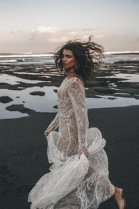 Bride running carefree on beach in long sleeve beaded lace wedding dress.