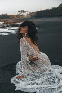 Bride sitting on beach posing wearing a backless beaded rock-and-roll wedding dress.